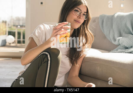 Giovane donna seduta sul pavimento a casa con un drink Foto Stock