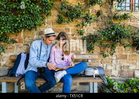 Una giovane coppia in una pausa in città, seduta su una panchina, guida di lettura Foto Stock