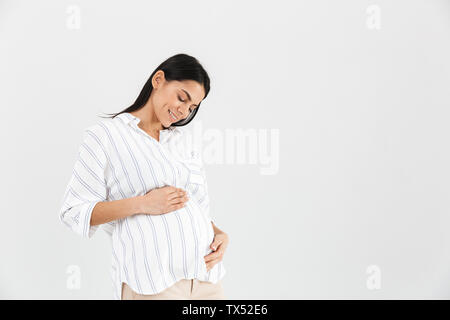 Immagine di gara donna incinta 30s sorridente e toccando il suo grande pancia mentre in piedi isolato su sfondo bianco Foto Stock