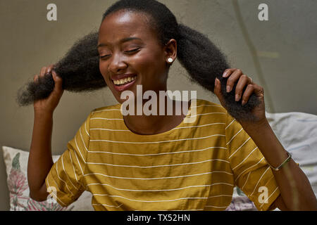 Donna felice con gli occhi chiusi a giocare con i suoi capelli Foto Stock