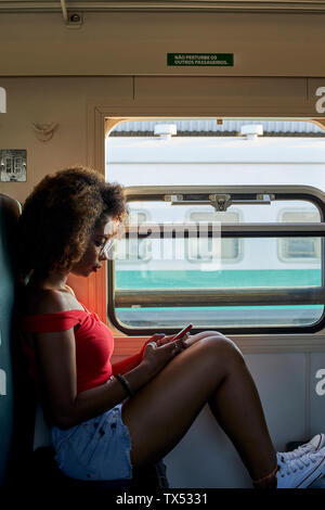 Giovane donna su un treno controllando il suo telefono Foto Stock