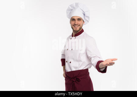 Immagine di sorridente giovane cuoco in uniforme in piedi isolato su sfondo bianco. Cercando di puntamento della telecamera Foto Stock