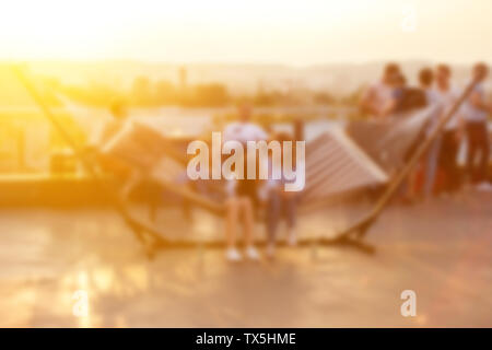 Defocalizzata persone che frequentano open air summer party sul tetto. Caldo sole di luce nella sera. Foto Stock