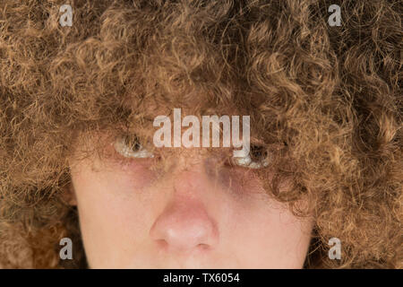 Ritratto di un giovane curly uomo europeo con un grave aspetto guardando i suoi capelli lunghi con i suoi occhi fino. molto rigogliosa ragazzo maschio capelli. arricciamento dei capelli per gli uomini. Foto Stock