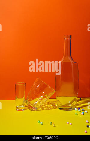La Pop art in stile di vita ancora con la bottiglia vuota e occhiali arancione e sfondo giallo Foto Stock