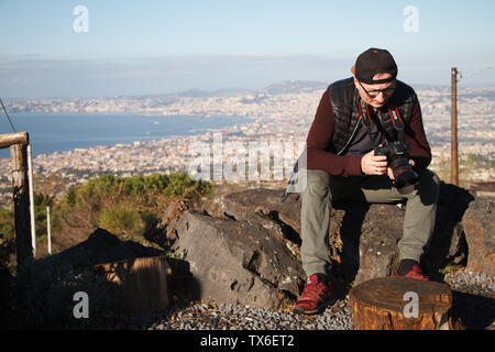 Napoli, Italia - 09 Novembre 2018: maschio adulto fotografo con una macchina fotografica in mano seduto sulla cima del Monte Vesuvio sullo sfondo della Napoli Foto Stock