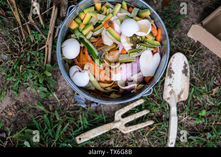 Vista aerea di variopinti scarti di cucina pronti per il compost in argento zincato benna con una vanga e cazzuola seduti nelle vicinanze. Foto Stock