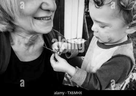 Immagine in bianco e nero di un bimbo piccolo ragazzo guardando le foto in un medaglione aperto appeso attorno a un adulto donna sorridente il collo. Foto Stock