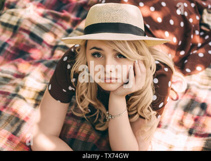 Riposo estivo Close-up verticale giovane donna bionda nel cappello di paglia e la polka dot dress è sdraiato sul plaid in una giornata di sole Foto Stock