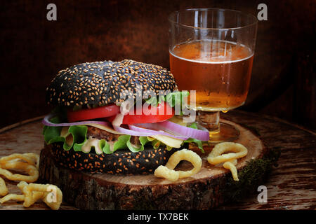 Burger di nero con birra e agli anelli di cipolla su uno sfondo di legno Foto Stock
