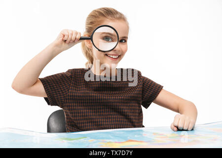 Ritratto di scuola europea ragazza guardando la mappa del mondo attraverso la lente di ingrandimento mentre studiava la geografia nella scuola isolate su sfondo bianco Foto Stock