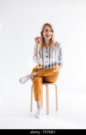 Foto di pensiero caucasica donna che indossa gli occhiali seduto in poltrona e tenere appunti isolate su sfondo bianco in studio Foto Stock