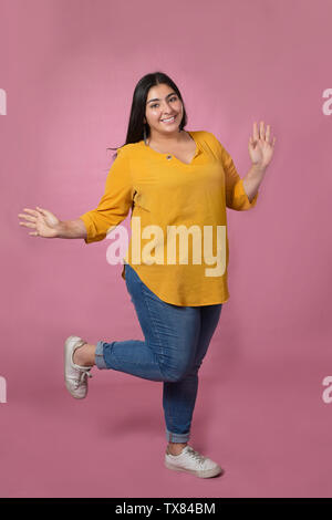 Chubby donna sorridente e felice con un abbigliamento informale che pongono il sollevamento di uno dei piedi e mani- ragazza latina Foto Stock