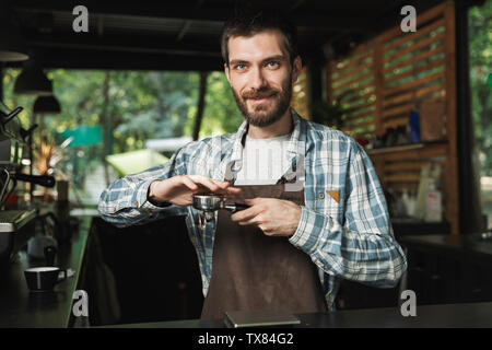 Ritratto di attraente barista uomo indossando grembiuli preparare un caffè mentre si lavora in street bar o caffetteria all'aperto Foto Stock