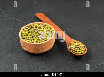 Verde fagioli mung in ciotola di legno e cucchiaio su sfondo scuro Foto Stock