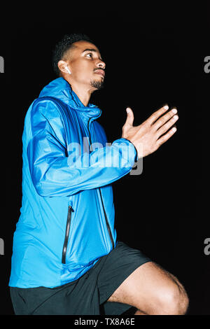Fiducioso montare i giovani africani uomo sportivo indossando giacca a vento esercizio all'aperto di sera e in esecuzione in spiaggia Foto Stock