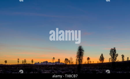 Glorioso tramonto nella natura con alberi in silhouette e il profilo delle montagne sullo sfondo, Kata Tjuta, Australia Foto Stock