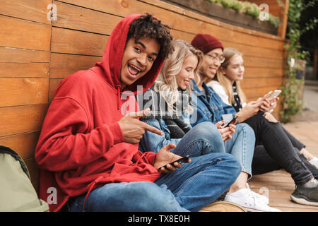 Felice multhietnic amici studenti appendere fuori insieme all'aperto, utilizzando i telefoni cellulari Foto Stock