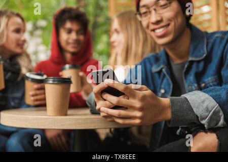 Felice multhietnic amici studenti appendere fuori insieme all'aperto, a bere caffè presso la caffetteria, chat Foto Stock