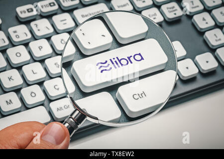 Lente di ingrandimento in mano maschio incentrata sulla chiave del computer con libra logo coin. cryptocurrency concept Foto Stock