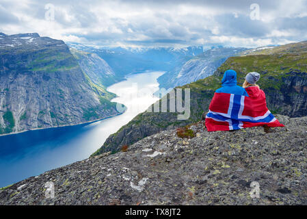 Giovane si siede sulla roccia e guarda alle montagne vicino Trolltunga. Popolare attrazione turistica. Ringedalsvatnet - lago nel comune di Odda in Hordalan Foto Stock