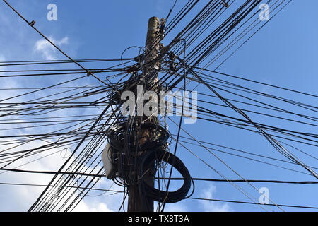 Vari tipi di cavi di alimentazione e i cavi di segnale, di linee telefoniche e linee di internet, sui poli di potenza. Cavo disordinati sul polo di calcestruzzo contro il cielo blu Foto Stock