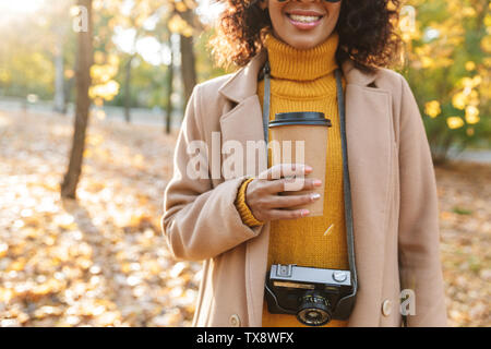 Immagine ritagliata di una giovane e bella donna africana passeggiate all'aperto in un parco di primavera di bere il caffè. Foto Stock