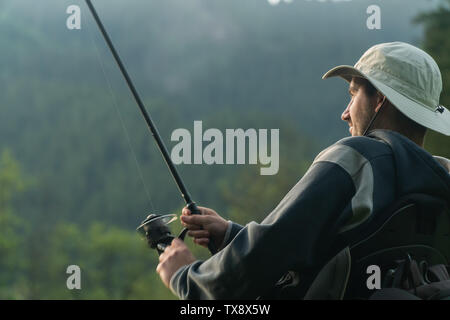 Giovane uomo su una sedia a rotelle la pesca al bel lago tramonto, alba Foto Stock