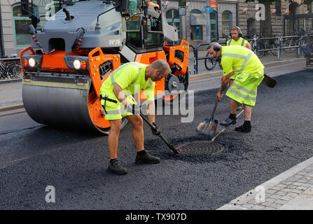 Karlstad, Svezia - 19 Giugno 2019: i lavoratori stradali asfaltatura manualy la zona intorno a un tombino. Foto Stock