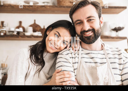 Immagine di adorabili giovane uomo e donna 30s indossando grembiuli abbracciando insieme durante la cottura in cucina a casa Foto Stock