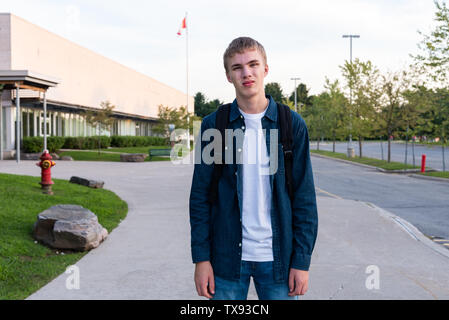 Sconvolto adolescente in piedi su un marciapiede con una high school in background. Foto Stock