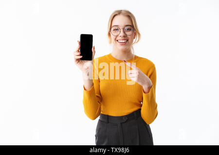 Bella ragazza che indossa un maglione in piedi isolato su sfondo bianco, puntare il dito a schermo vuoto del telefono mobile Foto Stock