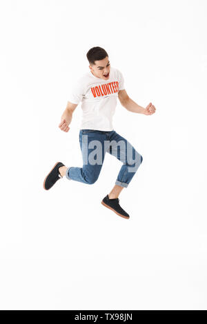 Per tutta la lunghezza od un felice giovane volontario che indossa la t-shirt jumping isolate su sfondo bianco, celebrando il successo Foto Stock