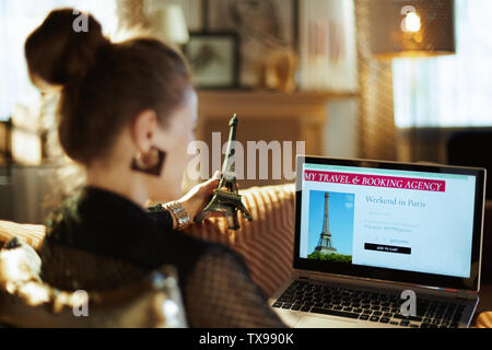 Sulla spalla colpo di elegante massaia in Blusa nera con la torre Eiffel ricerca hotel sul sito di prenotazione online seduti sul divano a casa moderna in su Foto Stock