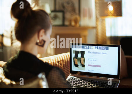 Sulla spalla colpo di donna elegante in nero camicetta seduti sul divano nella casa moderna in sunnny estate calda giornata di shopping scarpa nel negozio online. Foto Stock