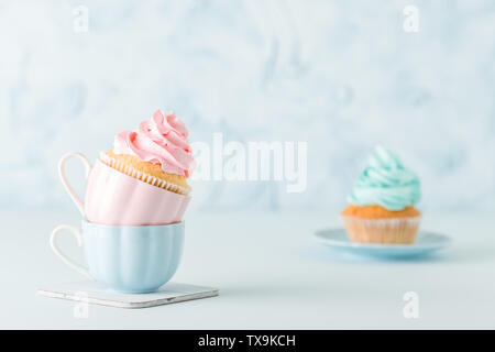 Tortine con delicata rosa e blu per la decorazione di crema in due tazze blu su sfondo color pastello. Banner orizzontale per matrimonio o compleanno invito, Foto Stock