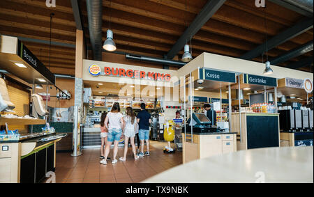 Stuttgart, Germania - 15 AGO 2018: Ampia Immagine vista posteriore del viaggiatore la famiglia presso il contatore di Burger King ristorante al distributore Esso in Germania in attesa di mettere ordine e ottieni il fast-food lontano Foto Stock