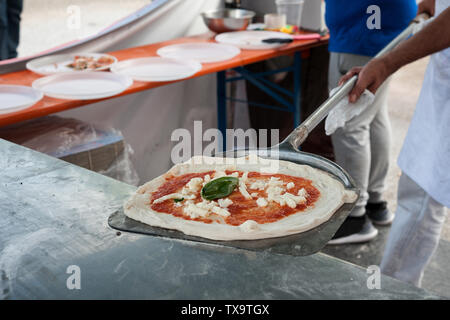 Preparare la Pizza Margherita sul bancone. Pizzaiolo mette impasto per pizza sulla buccia. Messa a fuoco selettiva Foto Stock