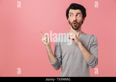 Allegro attraente giovane barbuto brunette man standing isolate su sfondo rosa, presentando uno spazio di copia Foto Stock