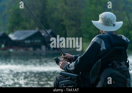 Giovane uomo su una sedia a rotelle la pesca al bel lago tramonto, alba Foto Stock