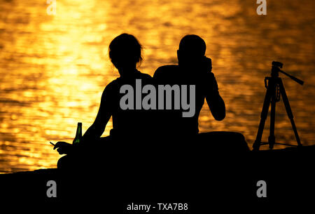 Hannover, Germania. Il 24 giugno 2019. Un giovane si siede nella luce del sole di setting presso il Maschsee e fotografie la sera dell'umore. Credito: Hauke-Christian Dittrich/dpa/Alamy Live News Foto Stock