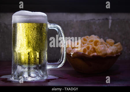 Congelati un boccale di birra con schiuma versando su di un legno rosso tabella con gli snack fritti Foto Stock