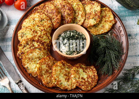 Frittelle di zucchini sono disposti su una piastra, al centro vi è la panna acida Salsa con aglio e aneto, la foto in orizzontale Foto Stock