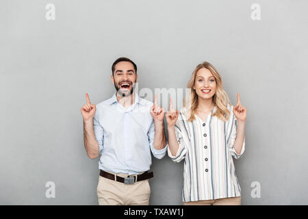 Foto della bella coppia in abbigliamento casual sorridere mentre le dita di puntamento a copyspace isolato su sfondo grigio Foto Stock