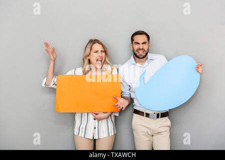 Attraente arrabbiato coppia giovane standing isolate su uno sfondo grigio, tenendo vuoto fumetti Foto Stock