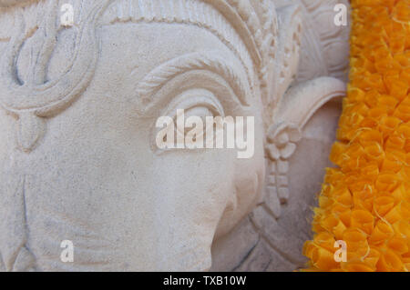 Colpo alla testa di un bel bianco Ganesha statua di pietra decorata con una ghirlanda di fiori di arancio e Situato in Ubud, Bali - Indonesia Foto Stock