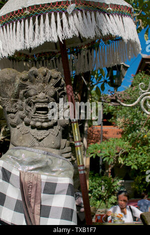 Ubud, Bali, Indonesia - 5 Maggio 2019 : Bedogol Balinese (noto anche come Dwarapala) pietra custode statua con donna Balinese in background mentre pl Foto Stock