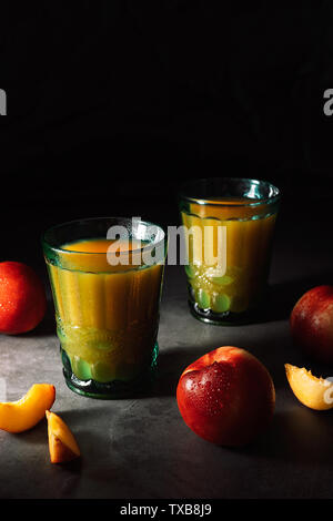 Still Life di prodotti freschi dolci le pesche noci con goccioline di acqua e succo di frutta in turchese vintage occhiali su sfondo scuro. Tasto basso. Foto Stock