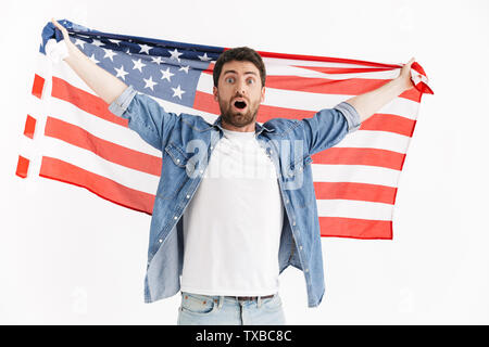 Ritratto di un entusiasta bello uomo barbuto indossando abiti casual in piedi isolato su sfondo bianco, indossa una bandiera americana Foto Stock