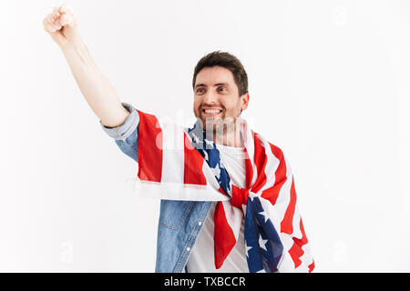 Ritratto di un entusiasta bello uomo barbuto indossando abiti casual in piedi isolato su sfondo bianco, indossa una bandiera americana Foto Stock